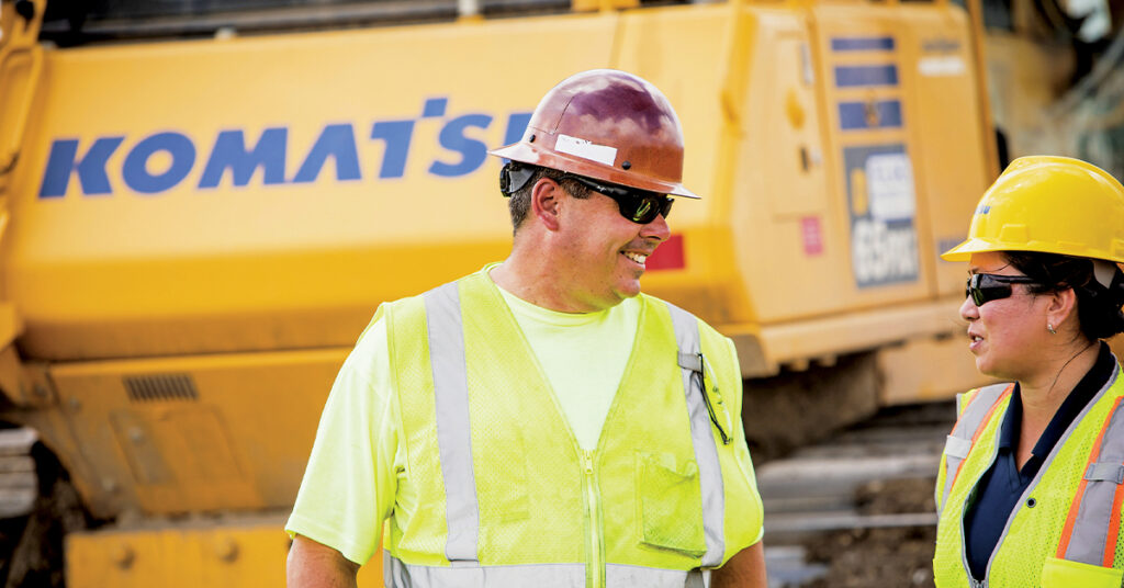 Hot Weather Safety Tips: A man and a woman working on a construction job site in the heat in front of a Komatsu D65PXi
