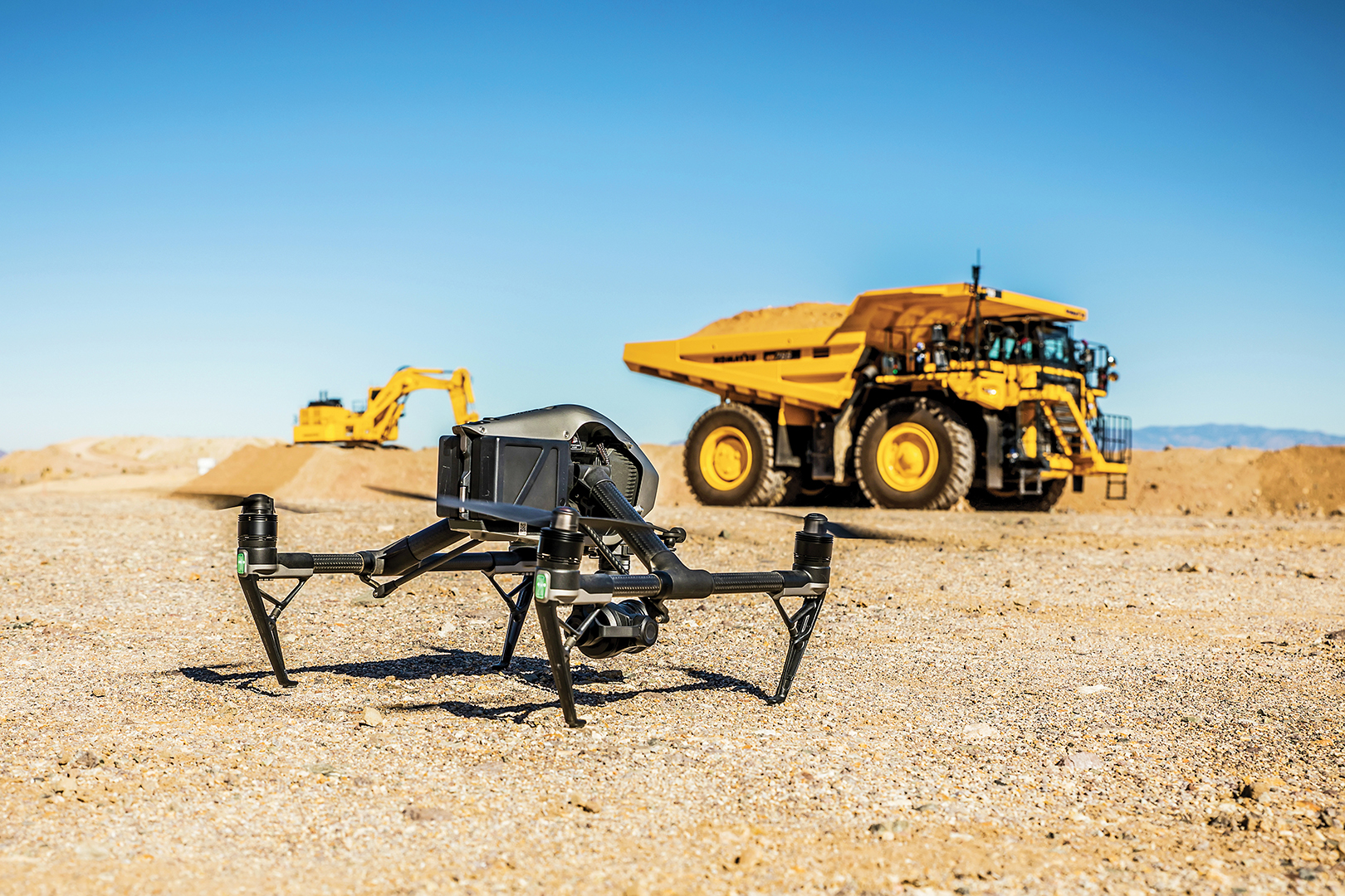 A drone sits in focus in front of an out of focus Komatsu Mining Truck and Komatsu Excavator