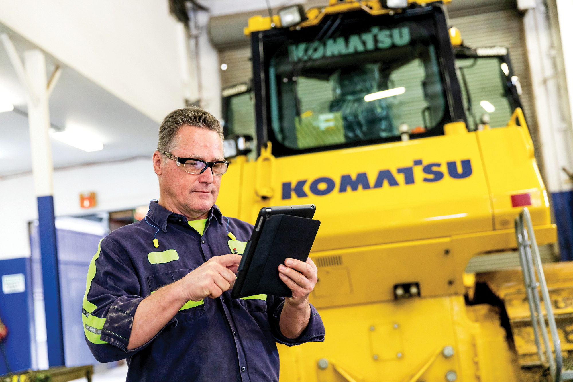 A man using an iPad in front of a Komatsu machine during a preventative maintenance clinic