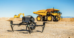 A drone sits in focus in front of an out of focus Komatsu Mining Truck and Komatsu Excavator