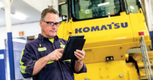 A man using an iPad in front of a Komatsu machine during a preventive maintenance clinic