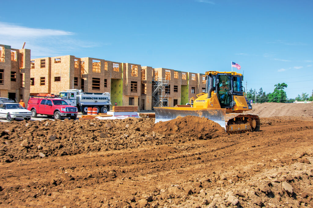 A Komatsu dozer moving dirt in front of a housing construction site