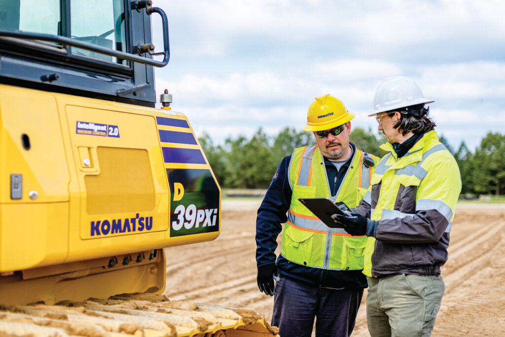 An image of certified technicians looking at a tablet in front of a Komatsu D39PXi dozer