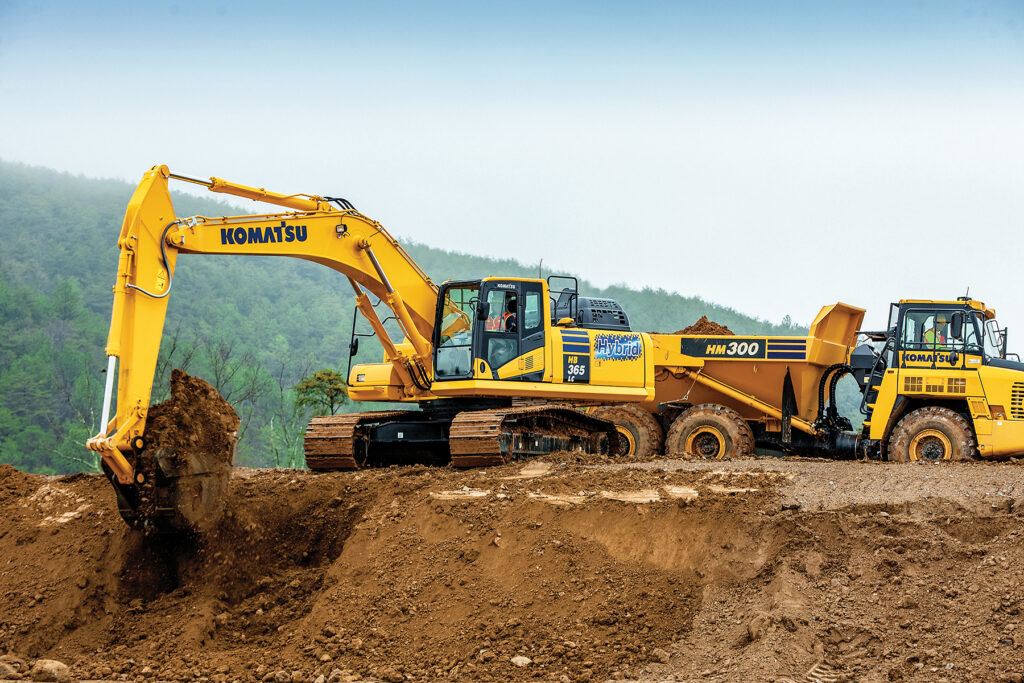 A Komatsu Hybrid HB365LC-3 Excavator moving dirt next to a Komatsu HM300 Truck