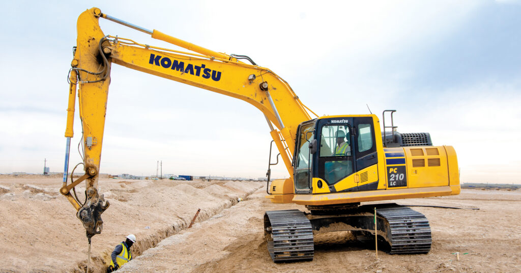 Construction workers working in a trench along with a Komatsu PC210LC excavator