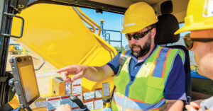 Two men in a Komatsu PC490LCi excavator with one pointing at the display