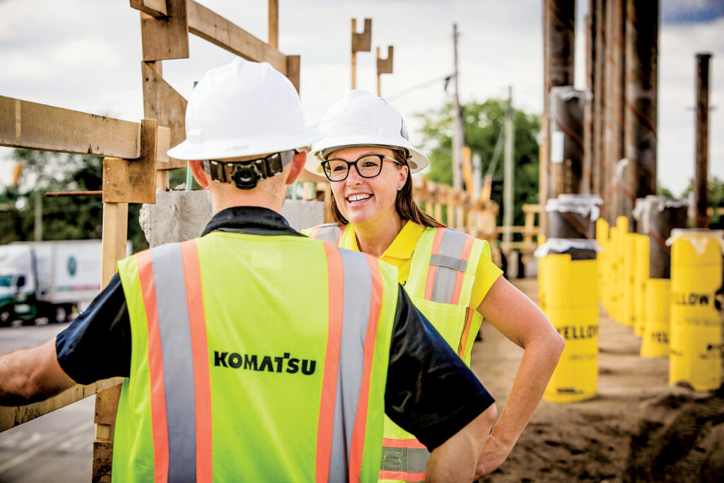 Two construction workers in Komatsu safety vests talk at a job site