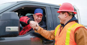 Culture in Construction showcased with two men, one in a truck, and the other outside the truck and wearing a hard hat and safety vest shaking hands through the truck window