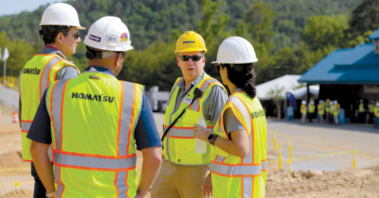 A group of four people, including three men and one woman, all wearing Komatsu hard hats and reflective vests. This is highlighting that it is important to speak up to stay safe.