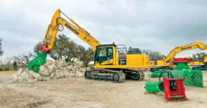 An attendee operates a Komatsu PC360LC-11 excavator with a straight boom equipped with a Lehnhoff SQ80V fully automatic symmetric quick coupler and a Montabert HCP 1000-R pulverizer. Other attachments surround the excavator.